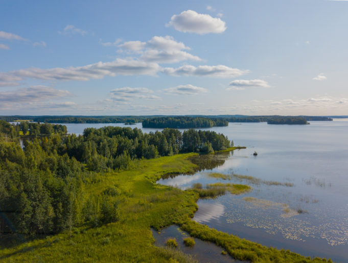 Markluhdanlahti kesällä kuvattuna ilmasta käsin drone-kopterilla aurinkoisena kesäpäivänä. Markluhdanlahdella on metsää ja vihreää kasvillisuutta rannassa ja järvi on sininen. Taivaalla on valkoisia pilviä ja järvenselällä näkyy saaria.