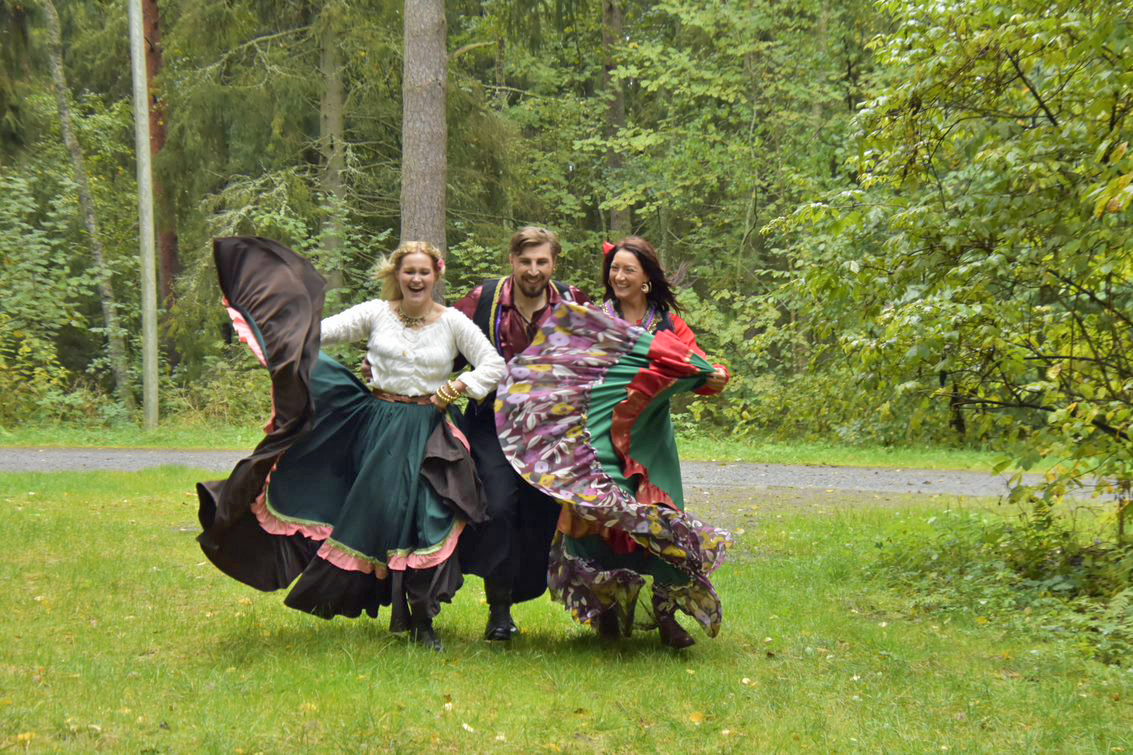 Romaninaisiksi ja -mieheksi pukeutuneita näyttelijöitä Kultaiset korvarenkaat -näytelmässä juoksemassa metsän siimeksestä.