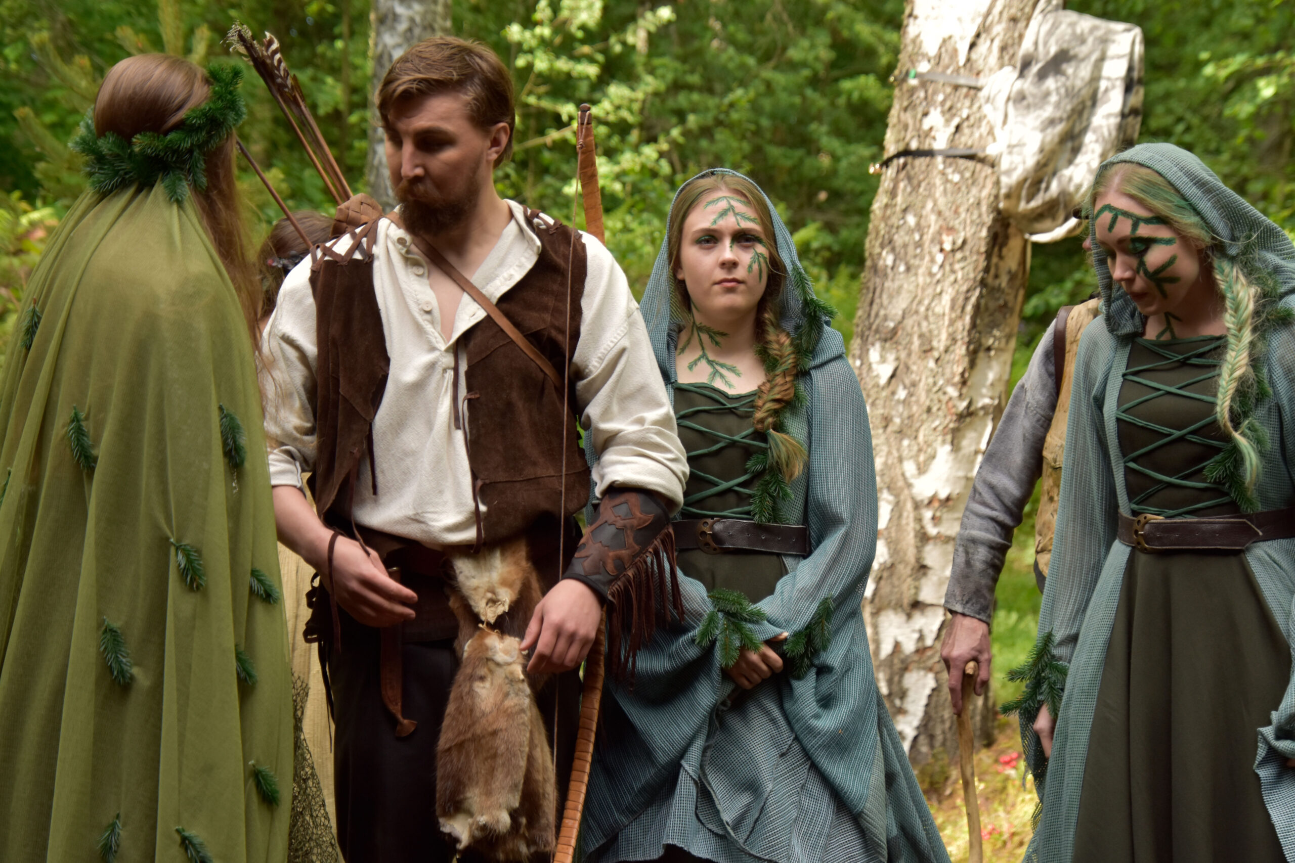 1800-luvun tyylisiin, vihreän ja ruskean sävyisiin pukeutuneet näyttelijät metsän keskellä.