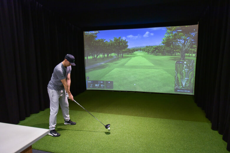 Mies harjoittelee golfia sisätiloissa simulaattorin avulla.