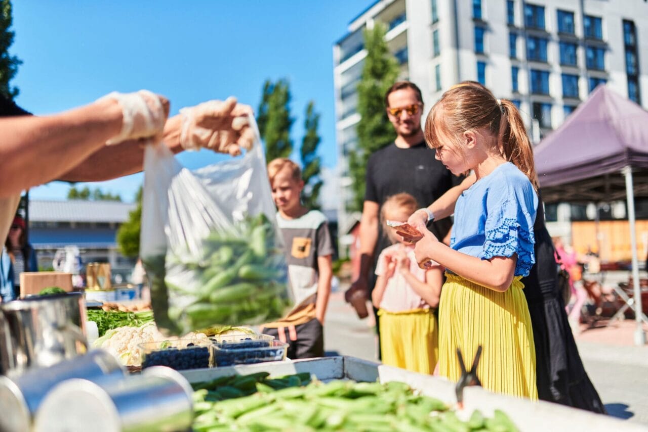 Aikuisia ja lapsia ostamassa herneitä torikauppiaalta